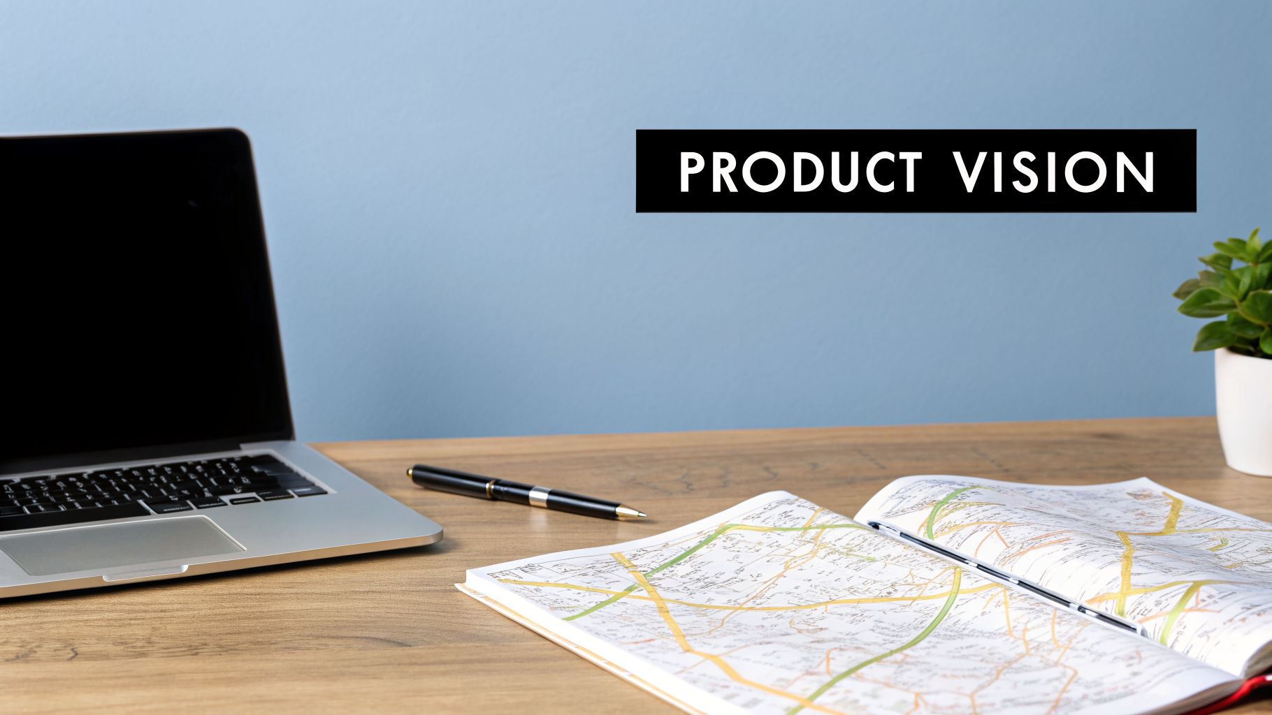 A desk setup with a laptop, pen, open map book, and plant, featuring 'PRODUCT VISION' text on a blue wall.