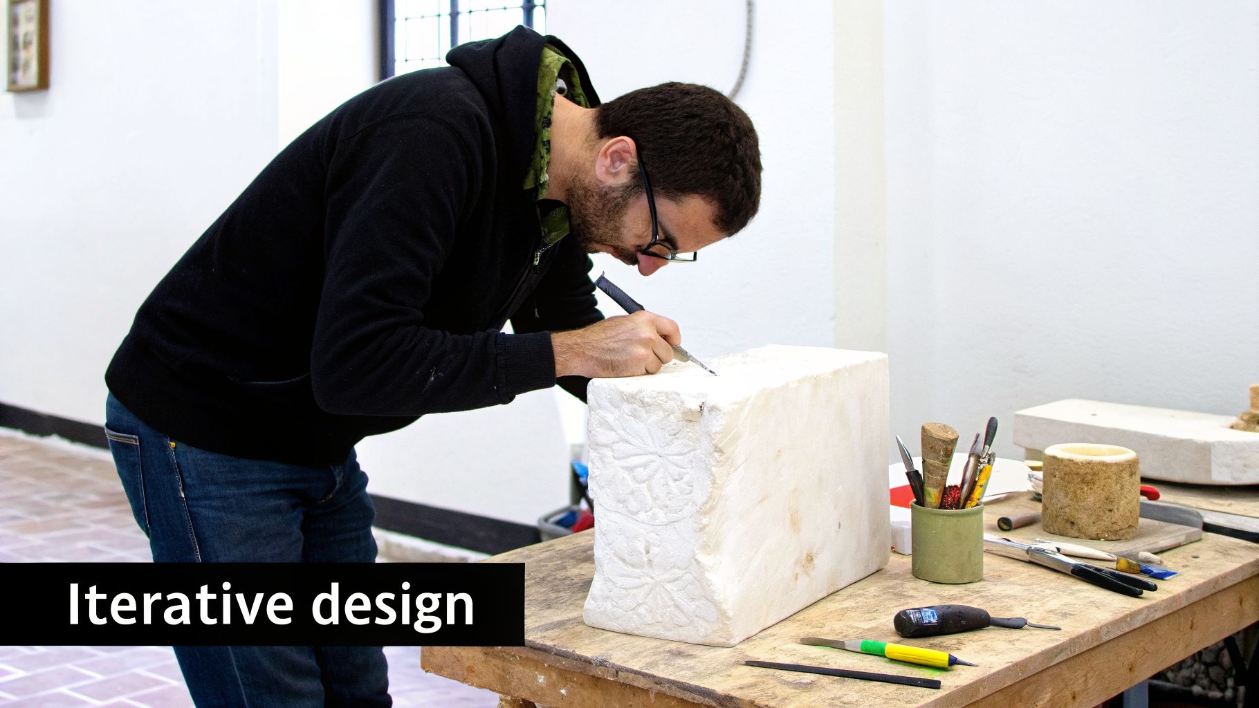 A man with glasses meticulously carves a decorative pattern into a white stone block.