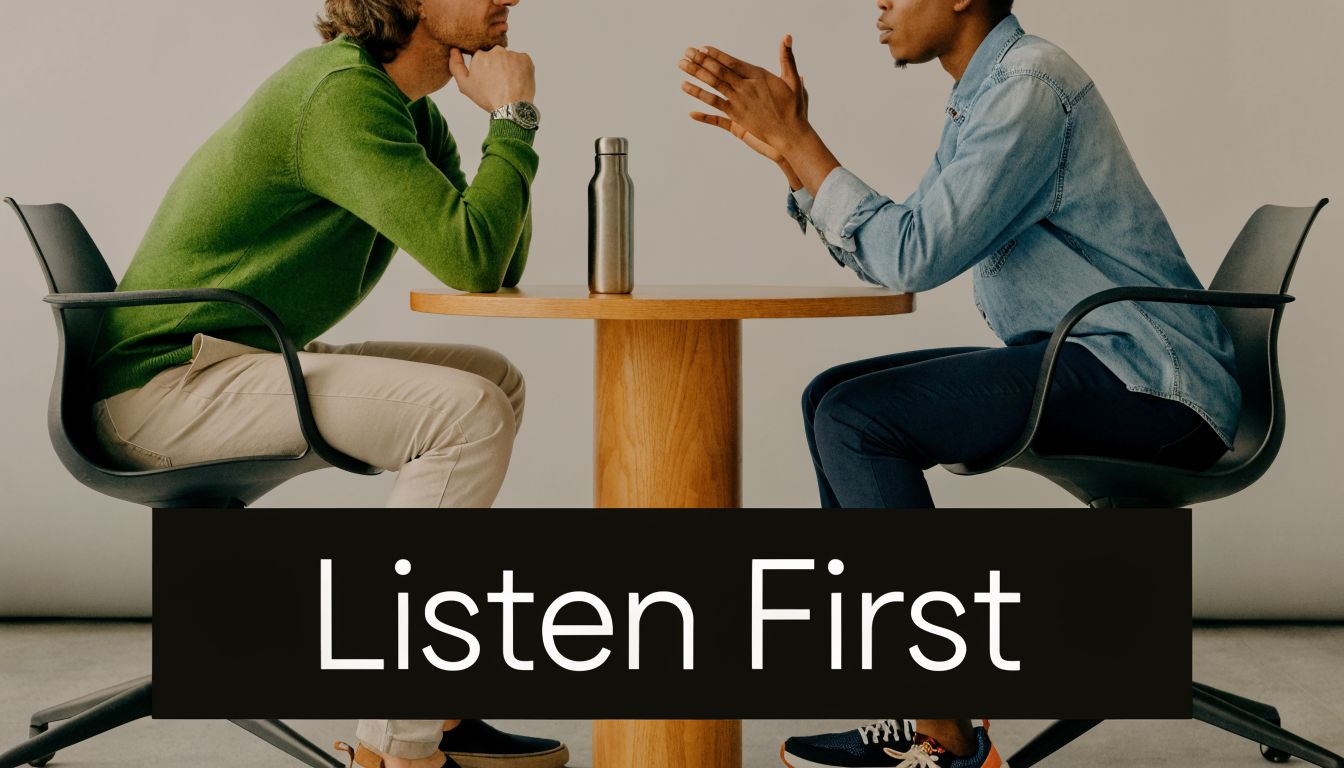 Two professional colleagues sitting at a table having a serious conversation about management with Listen First text.