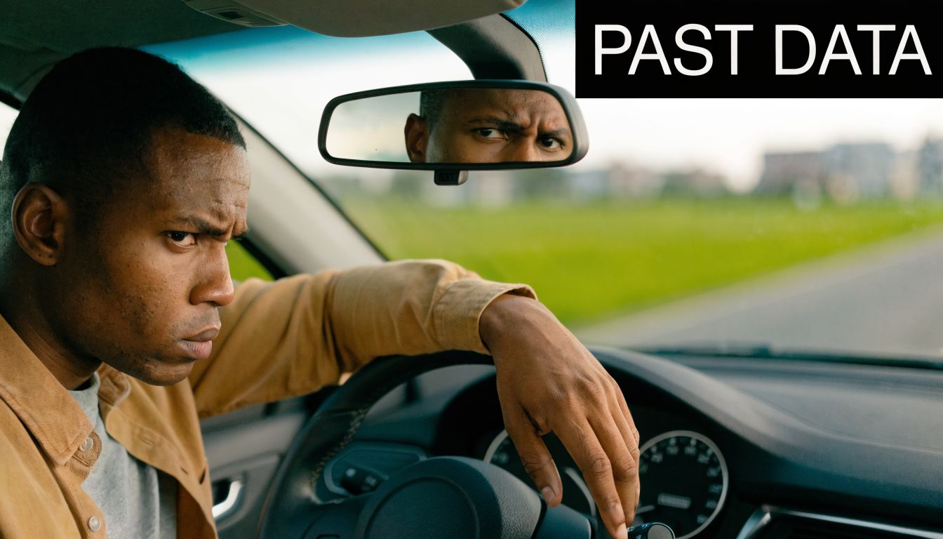 A focused man driving a car while looking into the rearview mirror, representing past data analytics.