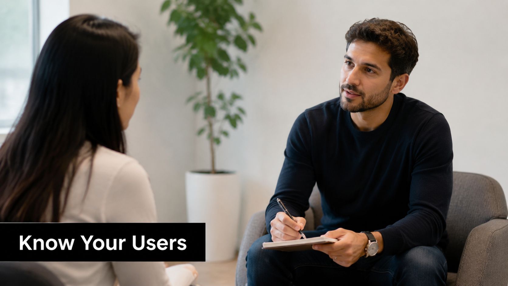 A professional man taking notes while interviewing a woman in a bright modern office setting.